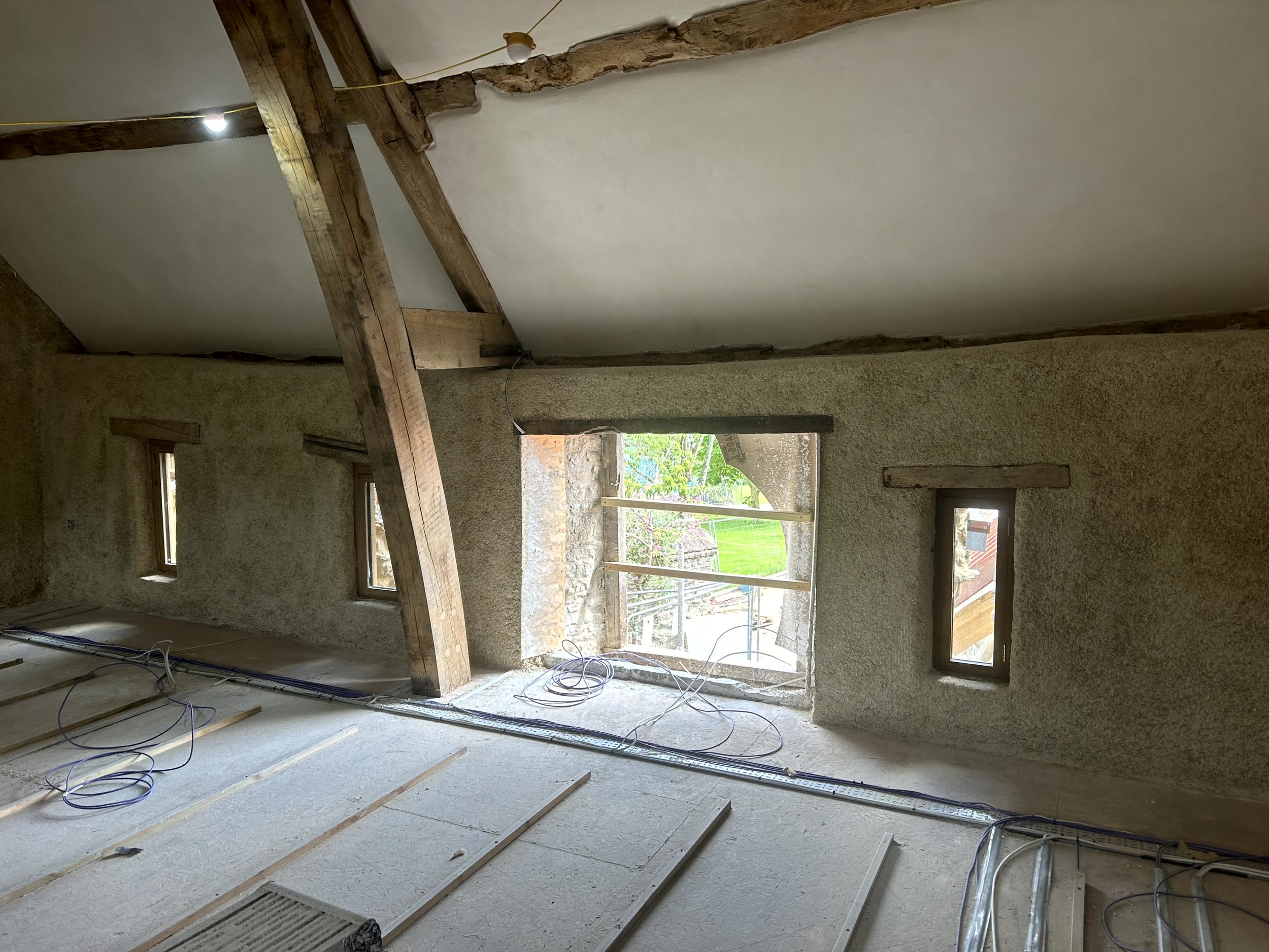 Sprayed hempcrete on the gable end wall, following the line of two small windows and a central window looking out to trees