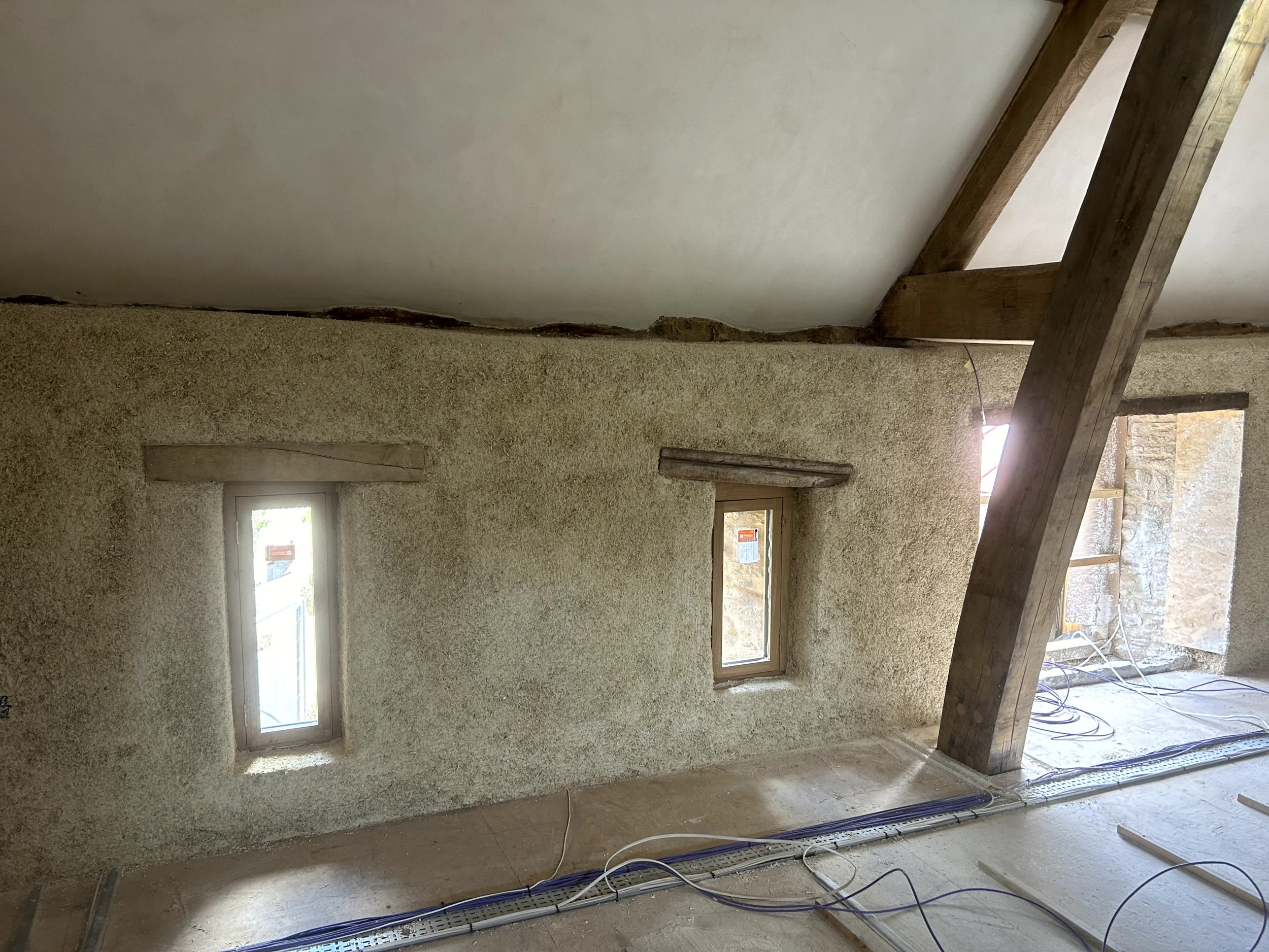 Sprayed hempcrete covering the full triangular gable wall up to the oak ridge truss, with a door reveal at the base