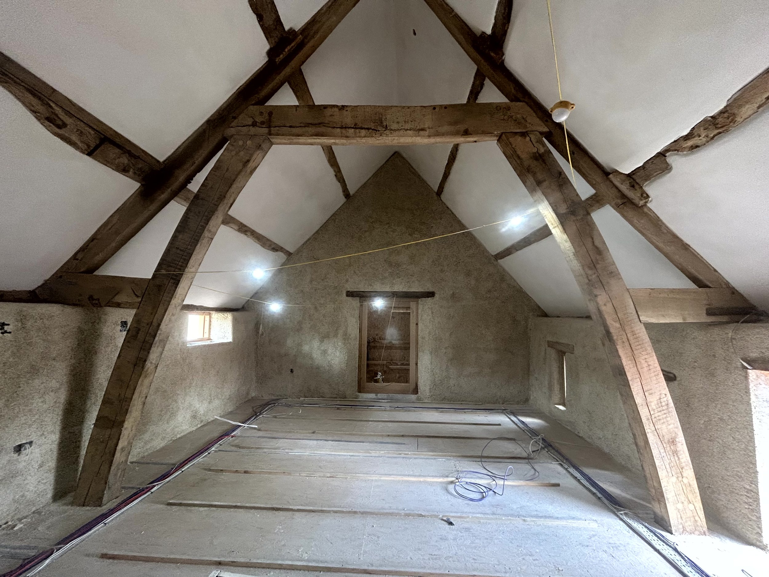 Sprayed hempcrete wall with two window reveals and a diagonal oak brace crossing in front of the finished surface
