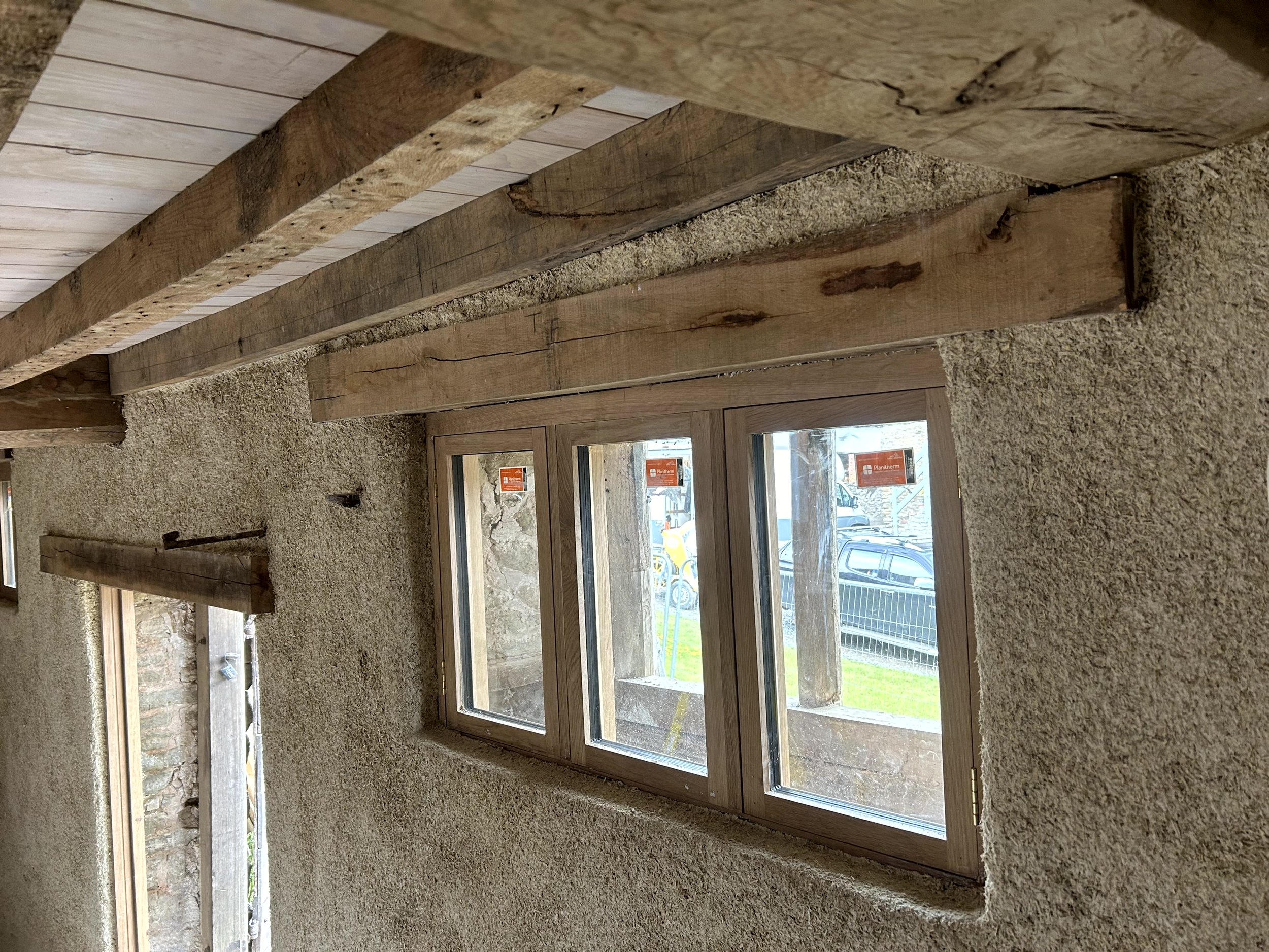Triple-casement window set into a finished hempcrete wall, with the original oak lintel left exposed above