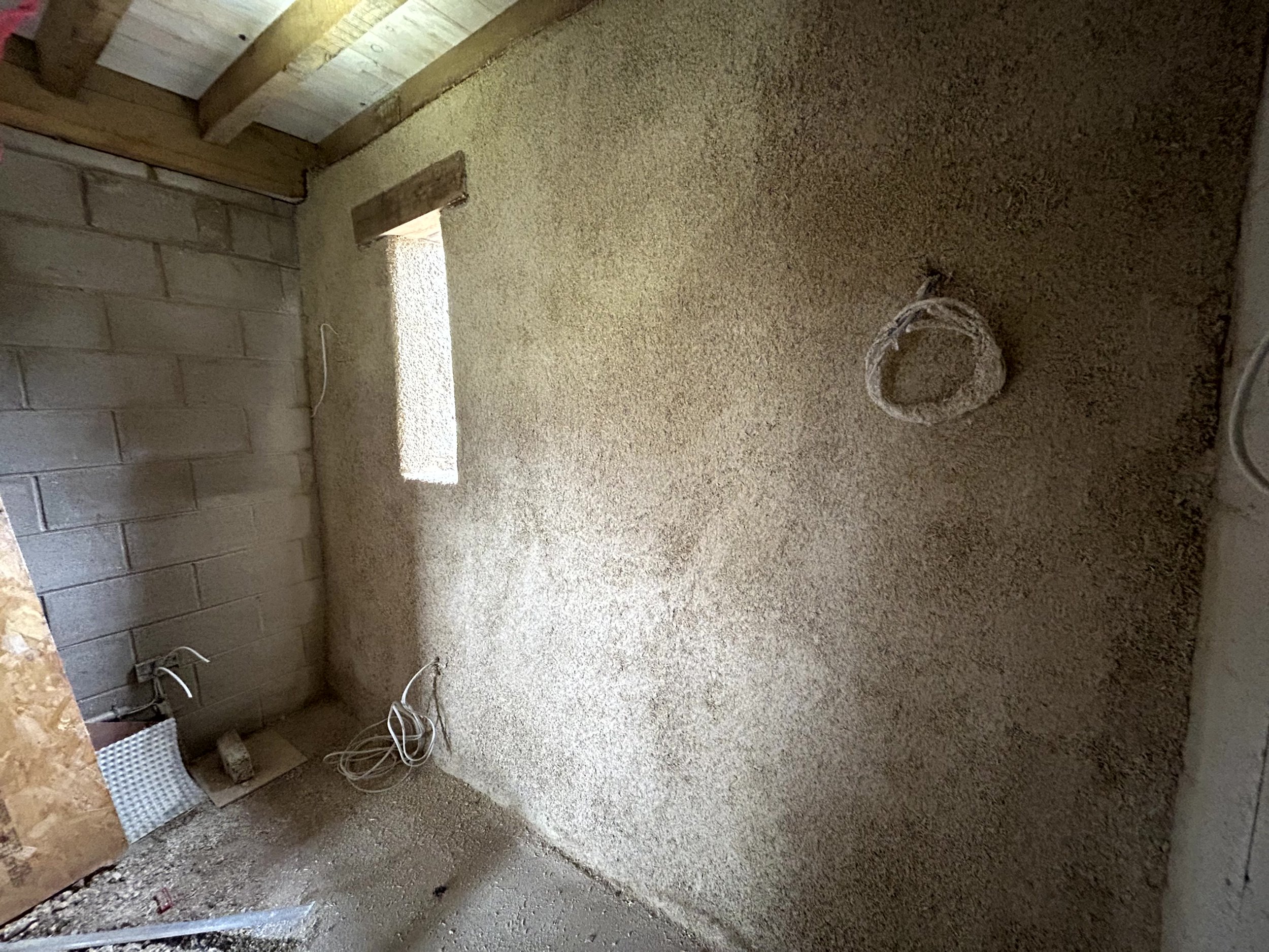 Corner where the hempcrete-finished wall meets a blockwork dwarf wall, small window and a coiled rope hung beside it