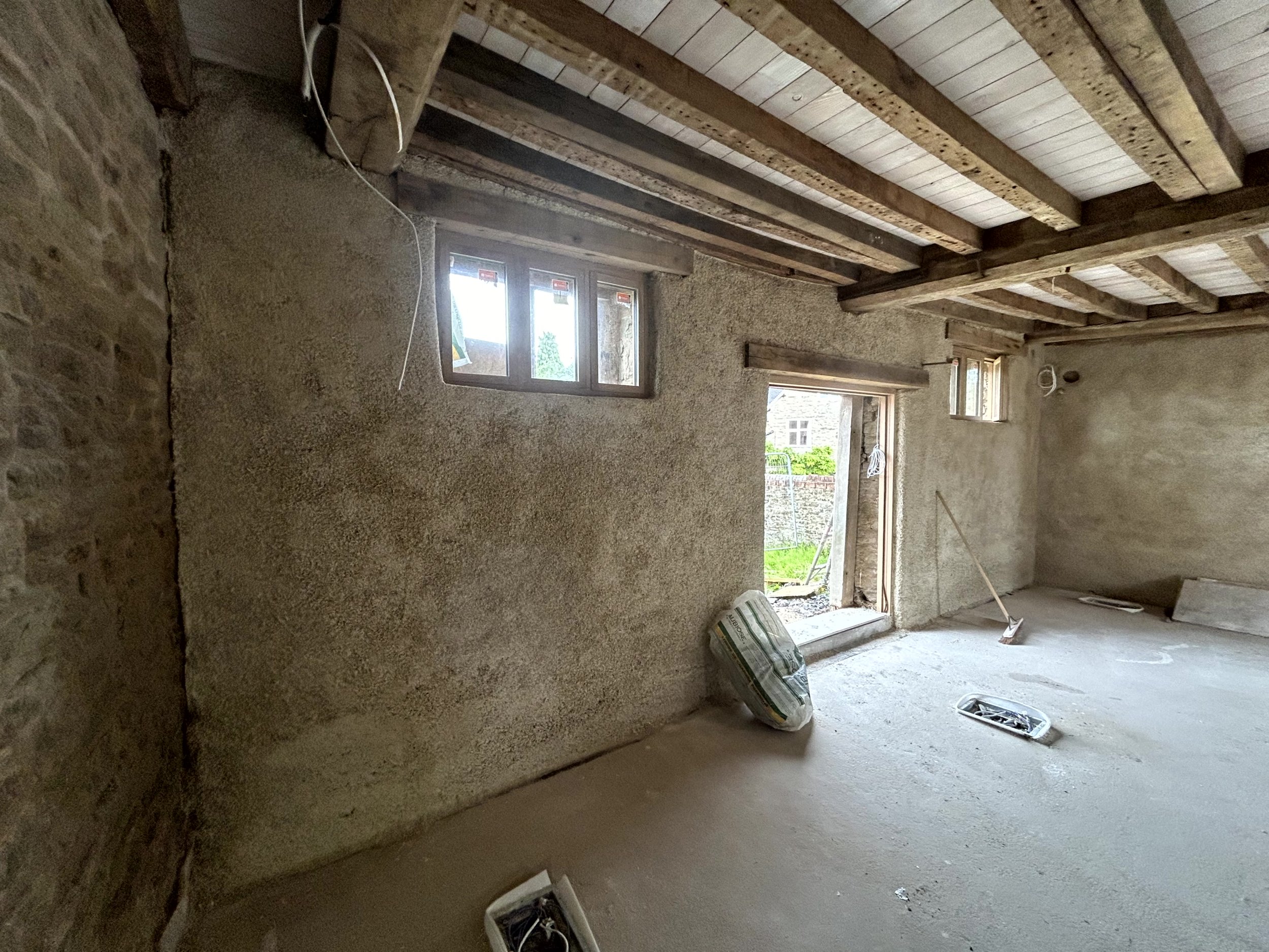 Finished room corner with bare stone on one side and a hempcrete-finished wall on the other, open doorway out to the garden