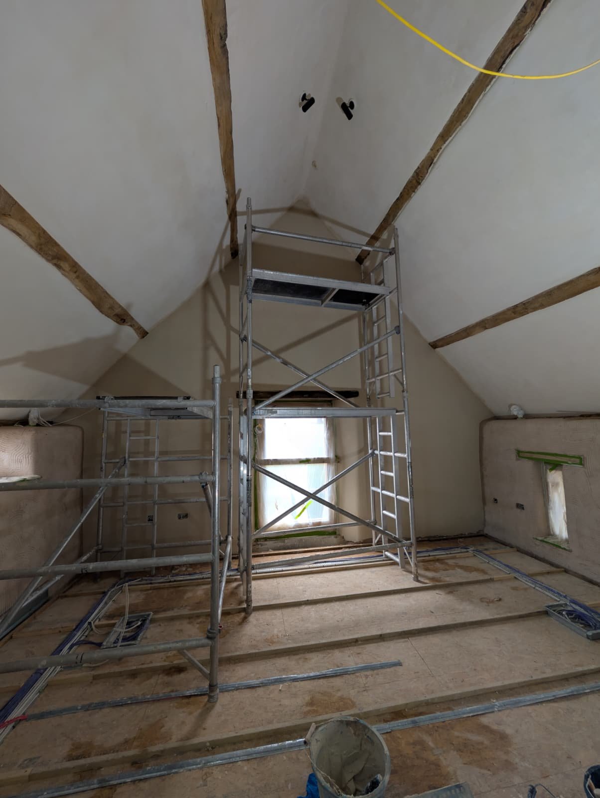 Tall access scaffold under the roof apex for finishing work, with masking tape protecting the window and door reveals either side